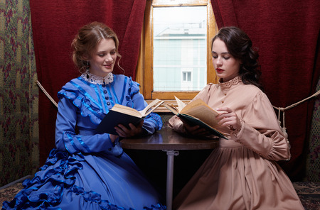 Two sisters in retro dress reading books in train compartmentの写真素材