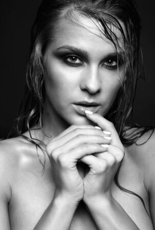 Portrait of young beautiful nude woman with wet shining  makeup  on black backgroundの写真素材