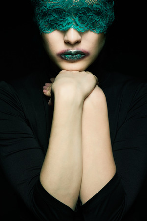 Halloween beauty portrait of young beautiful woman with green lacy ribbon on eyes on black backgroundの写真素材