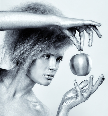 Portrait of girl with silver body art posing with shining apple in her hands on gray backgroundの写真素材