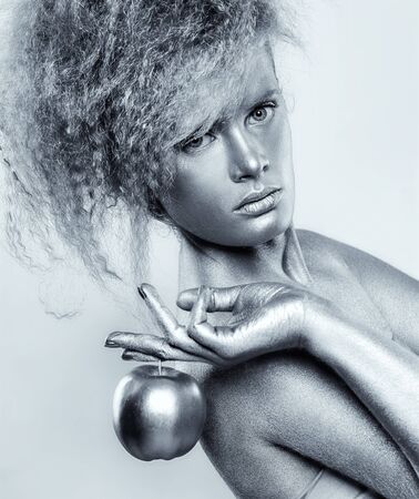 Portrait of girl with silver body art posing with shining apple in her hands on gray backgroundの写真素材