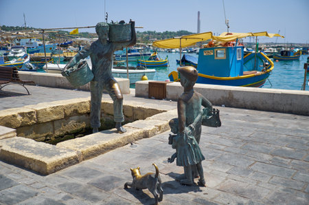 MARSAXLOKK, MALTA - AUGUST 2, 2015: The bronze statue of the fishermen on the harbour of village Marsaxlokk. The father returning from fishing with the haul is met by the son, daughter and cat. Maltaのeditorial素材