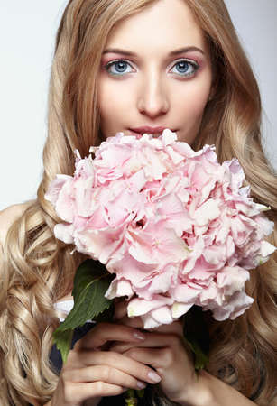 Closeup portrait of young beauty female face with blond hair and hydrangea bouquet flowers near face