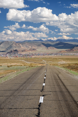 Empty Asphalt road in Mongolia  with mongolian town Bayan-Olgii (Bayan-Ulgii or Ulgii) on background under blue skyの写真素材