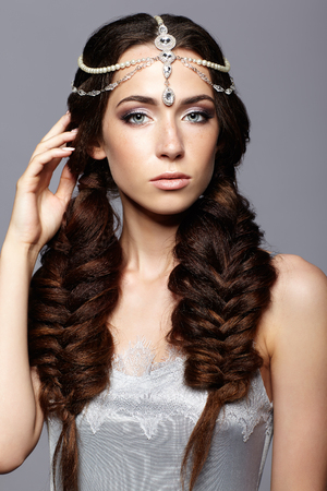 Beauty portrait of young woman with diadem. Brunette girl with long hair braids and day female makeup on gray background.の写真素材