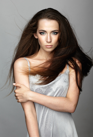 Beauty portrait of young woman. Brunette girl with long disheveled flying hair and day female makeup on gray background.の写真素材