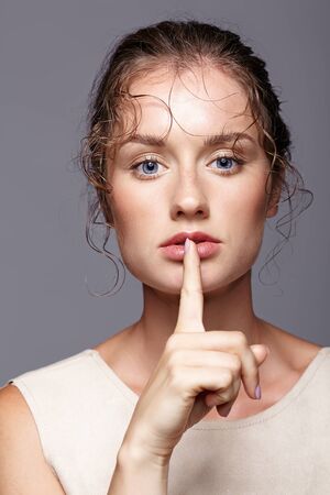 Young woman with finger over lips on gray background