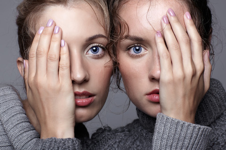 Two young women in gray sweaters on grey studio background. Beautiful girls stretching hands forward...