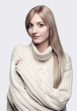 Blonde young beautiful woman dressed in large white cashmere sweater on gray backgroundの写真素材