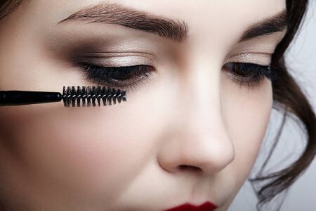 Close up portrait of beautiful young brunette woman face. Female applying mascara to eyelashes by...