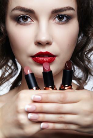 Portrait of young brunette woman. Girl with lipstick in hand. Female lips beauty makeup concept.の写真素材