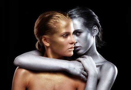 Beauty portrait of young gorgeous women. Golden and silver girls on black background.  Silver female hugging a golden oneの写真素材