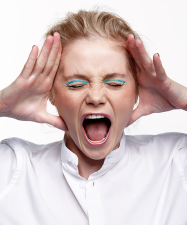 Emotional portrait of a young blonde woman on gray background. Female put palms to face and scream loudlyの写真素材