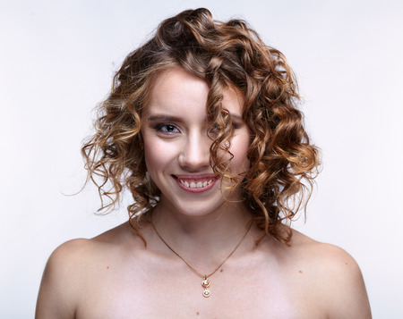 Smiling girl. Closeup beauty portrait of young woman. Female with curly hair on gray background.の写真素材