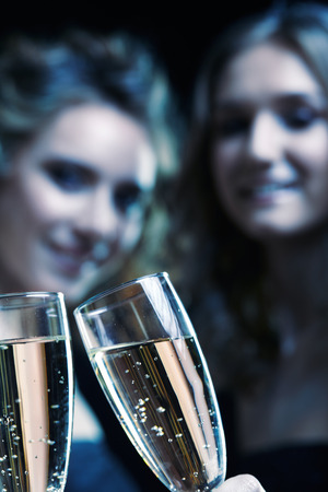 Two girls with glasses of champagne in their hands. Beautiful young women with vogue shining sparkle face makeup. Female Christmas portrait cinematic blue toned.の写真素材