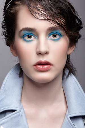 Portrait of female in blue jacket. Woman with unusual beauty makeup and wet hair. Girl with perfect skin, green pistachio colour eyes and blue shadows make-up.の写真素材