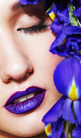 Closeup macro portrait of young beauty female face with unusual violet lips makeup and bouquet of irist flowers near face. Eyes closed.の写真素材