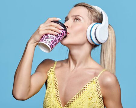 Young pretty happy woman drinking coffee and listening to music in headphones. Female in yellow...