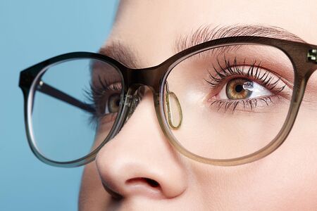 Close-up ortrait of attractive young woman in glasses. Female looking away on blue background.の写真素材