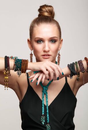 Beauty portrait of young female with hand up on gray background. Beautiful woman in collar necklace and multiple bracelets on hands.の写真素材