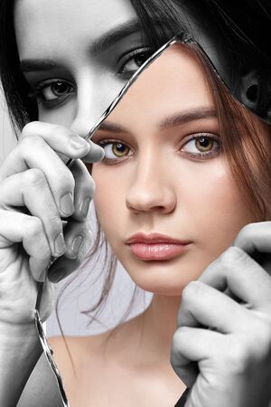 Monochrome portrait of girl with a shard of the mirror. Female with mirror shard in hand posing on...
