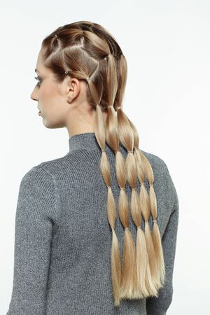 Back view portrait of beautiful young dark blonde woman. Female with creative braid hairdo on gray...