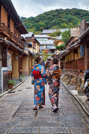 KYOTO, JAPAN - OCTOBER 18, 2019:  Two young Japanese girls in kimono walk along the street among the typical townhouses (machiya) buildings in the middle of Gion neighborhood. Kyoto. Japanのeditorial素材