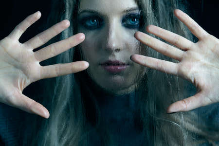 Young woman behind the window glass with raindrops. Female in gray sweater looking through the glass...