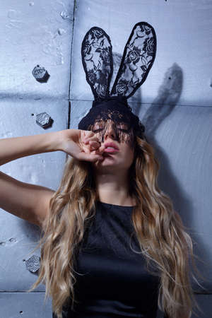 Young woman in black rabbit or hare fancy masquerade mask and black dress. Female holds hand near...