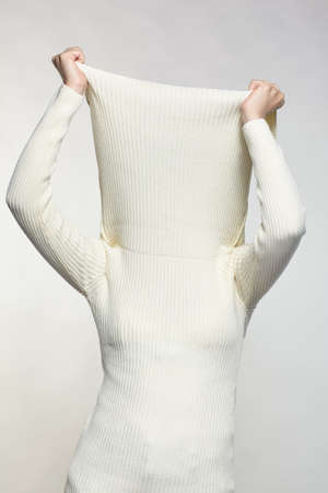 Woman dressed in large white woolen sweater on gray background. Female with hands on sweater collar...