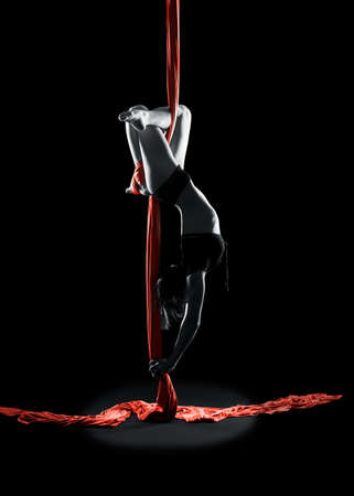 Young woman gymnast with red gymnastic aerial silks on black background