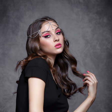 Beauty portrait of a young woman on gray background. Brunette girl with an oriental appearance with evening female makeup and black T-shirt. Rhinestone embellishment on the head.の写真素材