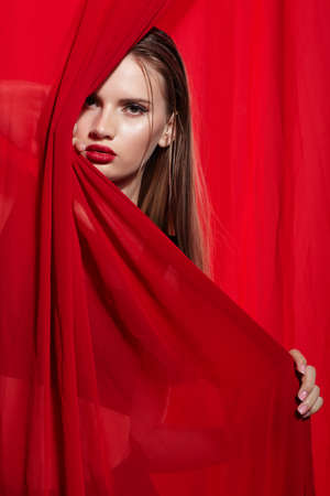 Portrait of young woman wrapped in red cloth. Hand near face. Hand near face.の写真素材