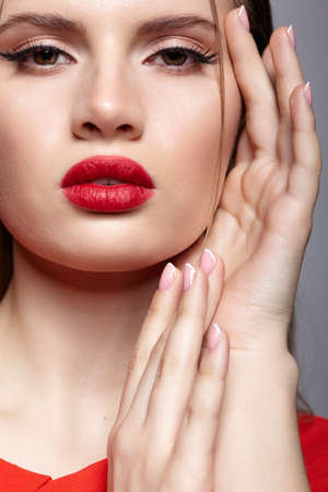 Portrait of young woman in red dress. Female beauty makeup concept and long earring with rhinestones in the ear. Hand near face.の写真素材