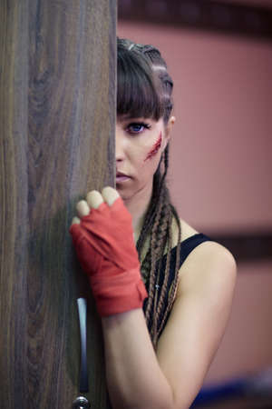Female fighter in the women's locker room. A woman with a boxing taping bandage on hand and an abrasion on her cheek peeks out from behind a locker door.の写真素材