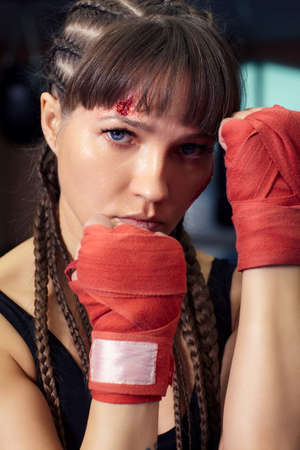Female fighter with boxing taping; bandage on her hands stands. Woman has an abrasion on her cheek.の写真素材