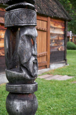Hitching post on background of ail house. Wooden post to which a horse is tethered to prevent it from straying, Carved from a log in the shape of a wooden idol's face.の写真素材