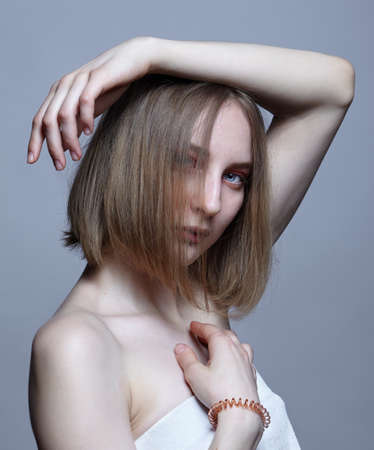 Close-up portrait of a beautiful young woman. Female with blond hair covering her face looks at the camera.の写真素材