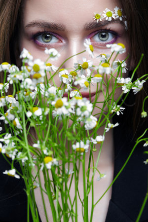 Female with long brown hair cher bouquet of daisies. Woman with brows decorated by small chamomile flowers.の写真素材