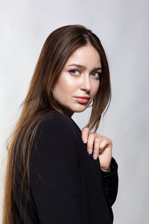 Woman in a black jacket. Female with long brown hair posing on gray background.の写真素材