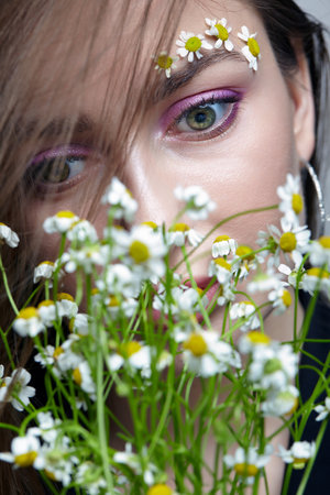 Female with long brown hair cher bouquet of daisies. Woman with brows decorated by small chamomile flowers.の写真素材