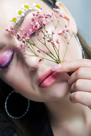 Close up portrait of female face with pink makeup. Woman with Gypsophila or babe's breath flowers in hand near face. Brows are decorated by small chamomile flowers. eyes closed.の写真素材