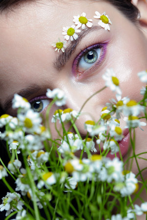 Female with long brown hair cher bouquet of daisies. Woman with brows decorated by small chamomile flowers.の写真素材