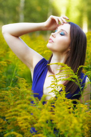 Romantic portrait of female in blue dress in nature. Brunette woman in the field of yellow flowers Solidago canadensis (Canada goldenrod or Canadian goldenrod) flowers. eyes closed.の写真素材