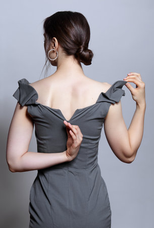 Young woman unzips the zipper on the dress. view from the back. Bunette female rear view with hair knot and earrings in the ears.の写真素材