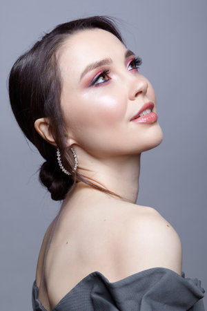 Portrait of young woman in gray dress on gray background. Bunette female side view with hair knot and earring in the ear.の写真素材