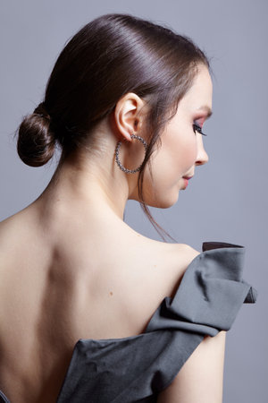 Young woman with unzipped zipper on the dress. view from the back. Bunette female rear view with hair knot and earrings in the ears.の写真素材