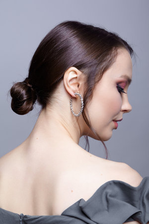 Portrait of young woman in gray dress on gray background. Bunette female side view with hair knot and earring in the ear.の写真素材
