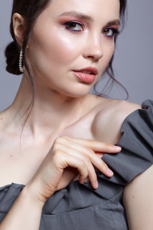 Portrait of young woman in gray dress on gray background. Bunette female side view with hair knot and earring in the ear. beauty makeup concept.の写真素材