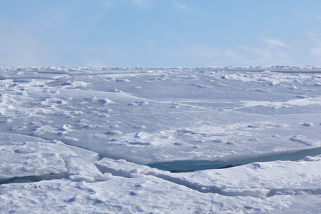 Winter ice landscape under blue sky and clouds. Cracks in the ice field. Natural winter background.の写真素材